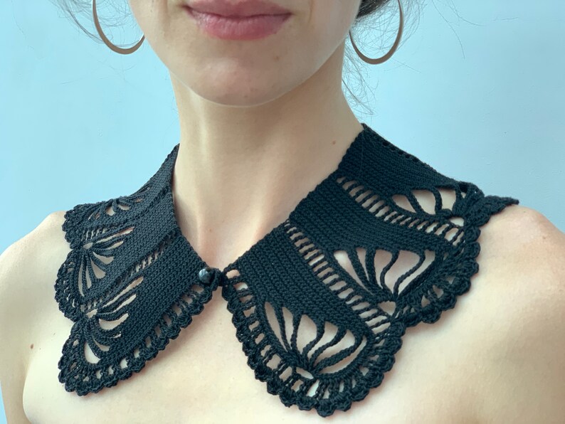 May include: A black crocheted collar with a delicate floral pattern. The collar is made with a fine yarn and has a button closure.