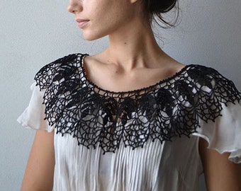 May include: A white blouse with a black crocheted collar. The collar is delicate and intricate, with a scalloped edge.