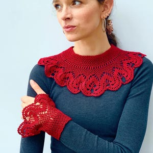 May include: A red crocheted collar and matching wrist cuffs. The collar is a wide, lacy design with a scalloped edge. The cuffs are shorter and have a similar lacy design.