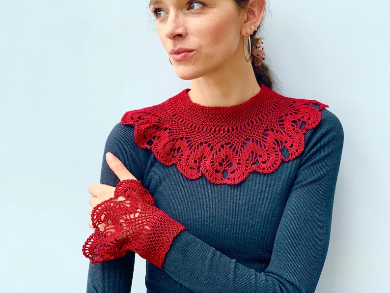 May include: A red crocheted collar and matching wrist cuffs. The collar is a wide, lacy design with a scalloped edge. The cuffs are shorter and have a similar lacy design.