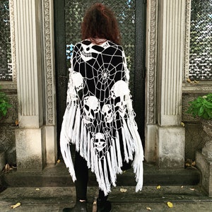 Pu&ograve; includere: Scialle in crochet bianco con un design a forma di teschio e ragnatela. Lo scialle ha frange lungo il bordo inferiore.