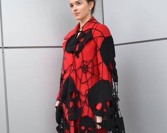 Può includere: Un cappotto rosso con un design a forma di teschio in pizzo nero. Il cappotto ha una silhouette lunga e fluida e un colletto alto.
