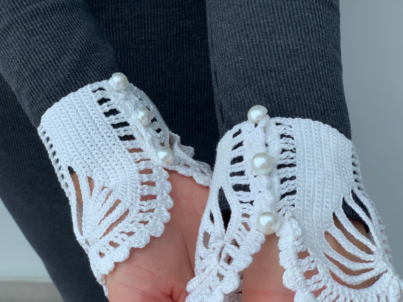 May include: A pair of white crocheted cuffs with pearl buttons. The cuffs are attached to a gray sweater.