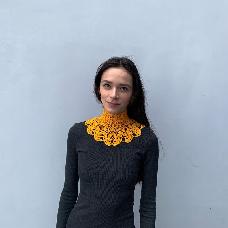 Puede incluir: Una mujer con un collar de ganchillo amarillo mostaza sobre una camisa negra de cuello alto.