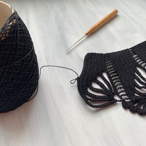 May include: Black crochet lace edging with a ball of black yarn and a wooden crochet hook on a white surface.