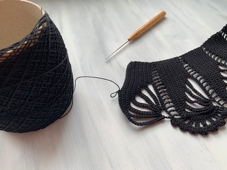 May include: Black crochet lace edging with a ball of black yarn and a wooden crochet hook on a white surface.