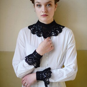 May include: A white button-up shirt with black crocheted lace trim around the collar and cuffs.