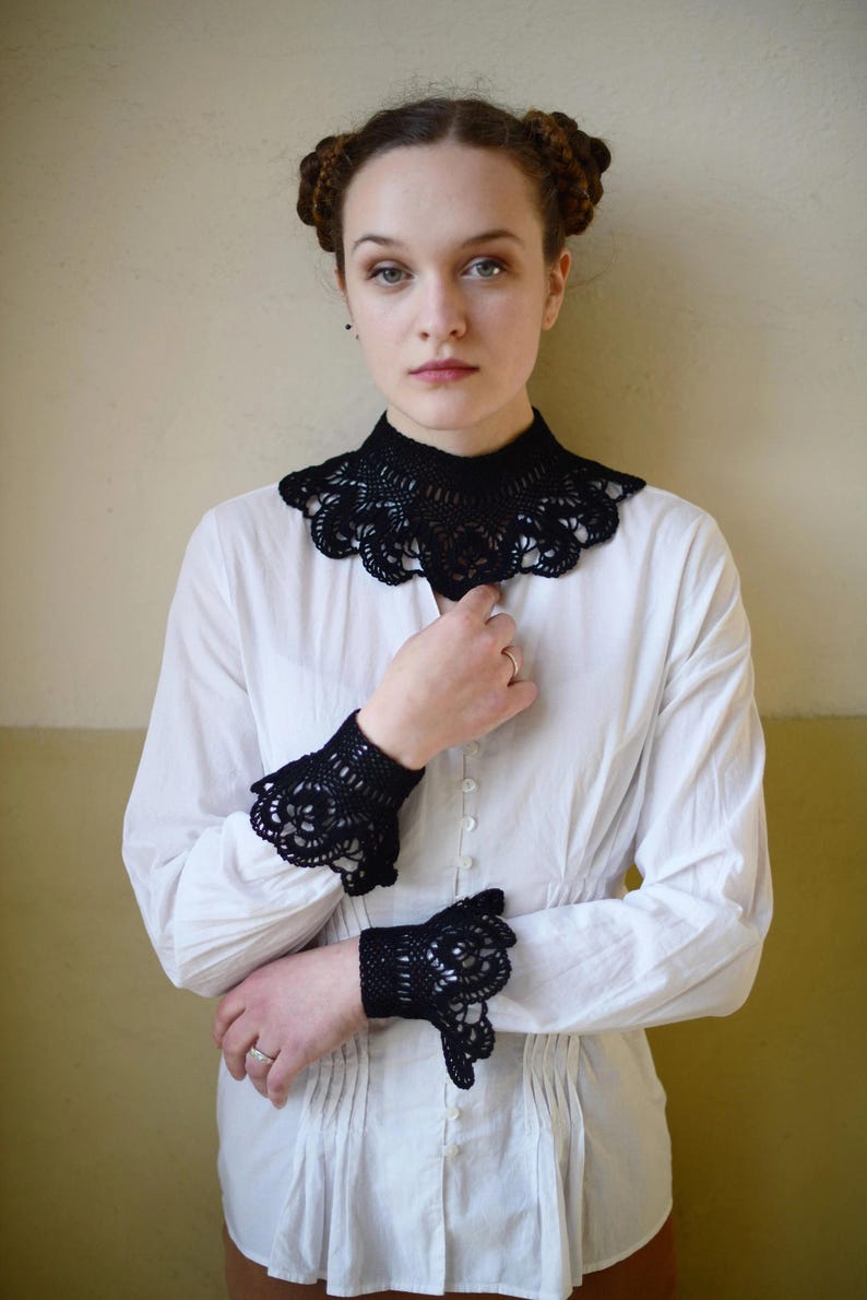 May include: A white button-up shirt with black crocheted lace trim around the collar and cuffs.