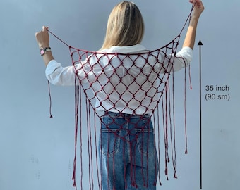 Può includere: Uno scialle in macramè rosso scuro con un motivo a rete annodata a forma di diamante e lunghe frange. Lo scialle misura 56 cm di larghezza e 90 cm di lunghezza, come indicato dalle frecce nere e dalle etichette di testo nell'immagine.