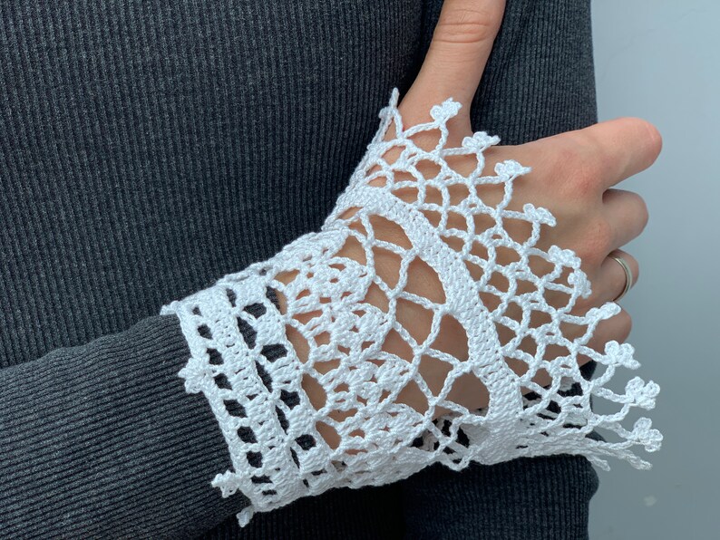 May include: White crocheted lace cuff with a delicate pattern. The lace is attached to a gray sweater sleeve.