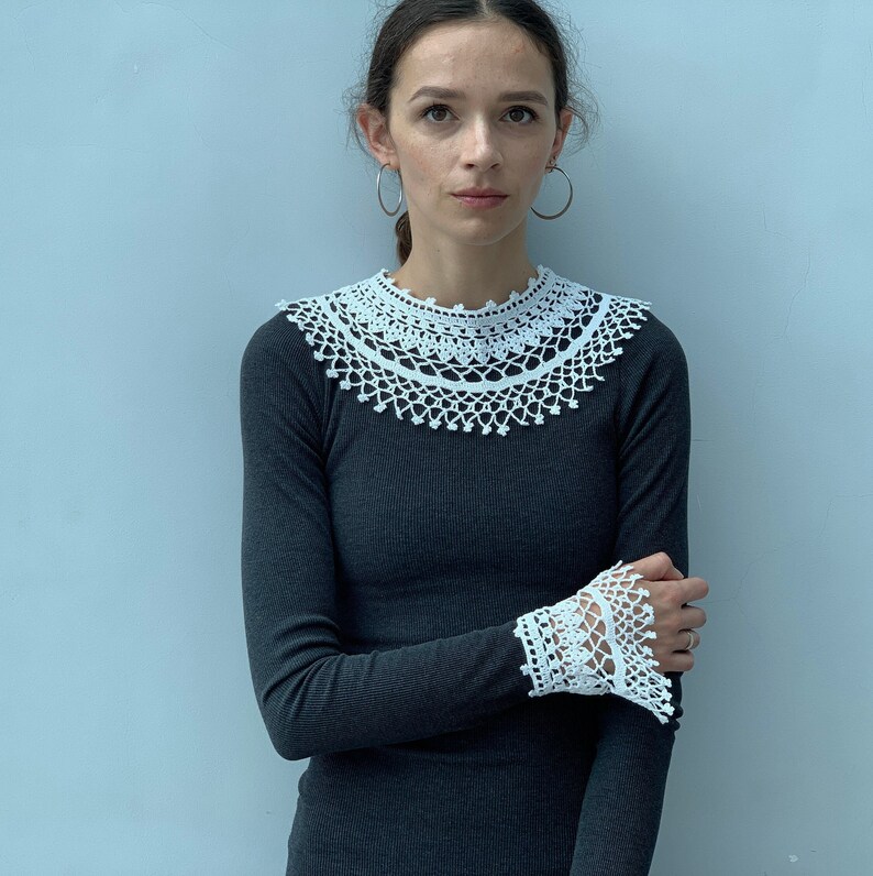 May include: A woman wearing a black long-sleeved shirt with a white crocheted collar and matching cuffs.