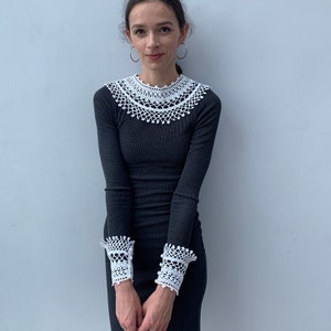 May include: A black long-sleeved dress with white crocheted trim around the neckline and cuffs.