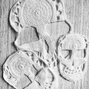 Pu&ograve; includere: Tre forme di teschio in crochet bianco, con dettagli intricati, sono disposte su una superficie in legno chiaro.