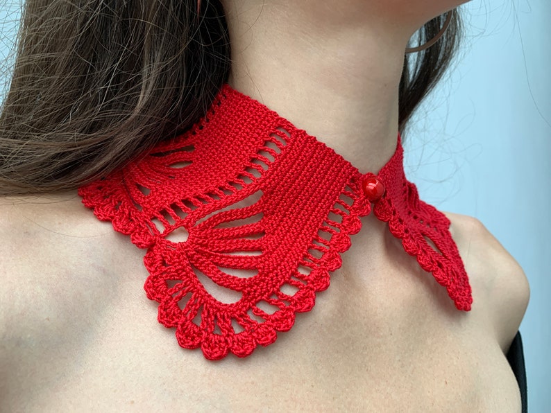 May include: A red crocheted collar with a decorative button. The collar is made with a delicate, lacy pattern.