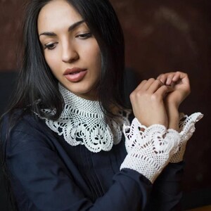 May include: A woman wearing a navy blue blouse with a white crocheted collar and matching cuffs. The collar and cuffs have a delicate floral design.