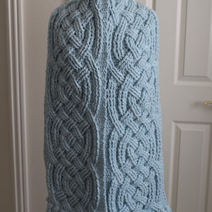 May include: A light blue crocheted shawl with a cable knit pattern and fringe trim.