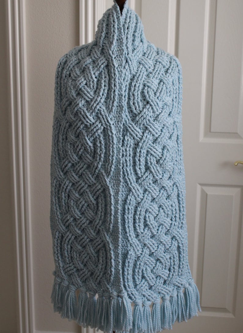 May include: A light blue crocheted shawl with a cable knit pattern and fringe trim.