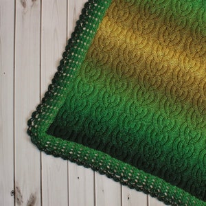 Op de afbeelding: Een groene en gele gehaakte deken met een gehaakte rand. De deken is gemaakt met een gradient garen dat van geel naar groen overgaat.
