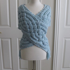 May include: A light blue crocheted shawl with a braided pattern and fringe. The shawl is displayed on a white mannequin.