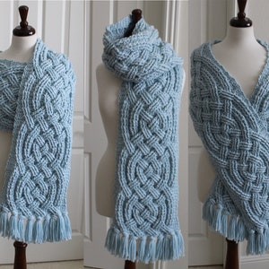 May include: A light blue knitted scarf with a Celtic knot pattern and fringe. The scarf is displayed on a mannequin in five different ways.