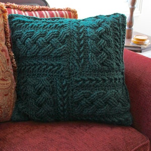 May include: A dark green knitted cushion with a textured pattern. The cushion is sitting on a red sofa.