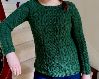 May include: A green knitted jumper with a cable knit pattern. The jumper has long sleeves and a round neckline.