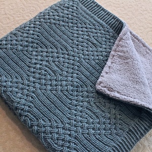 May include: A blue knitted throw blanket with a woven pattern and a soft, gray fleece lining.