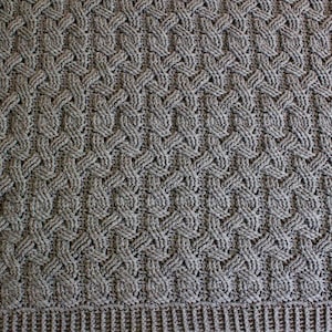 Peut inclure: Gros plan sur une couverture en tricot gris avec un motif en tricot torsadé.