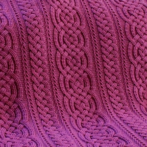 Peut inclure: Gros plan sur une couverture en tricot avec un motif en câble tricoté de couleur violet foncé.