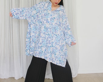 May include: An oversized shirt with a white and blue floral print, featuring a button-down collar and long sleeves. The shirt is worn with black wide-leg trousers.