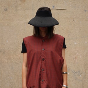 Può includere: Una camicia senza maniche a quadri rossi e neri con chiusura a bottoni e tasche. La camicia ha un colletto alla coreana.