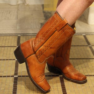 May include: A pair of brown leather cowboy boots with a woven pattern. The boots have a pointed toe and a high heel.