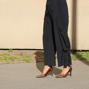 Peut inclure: Une personne portant un pantalon noir et des talons hauts à motifs rouge et noir.