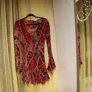 Peut inclure: Une robe à manches longues à motifs rouges et noirs avec des manches évasées est suspendue à un cintre noir. La robe a un col en V et un ourlet à volants. Le tissu a un motif zébré.