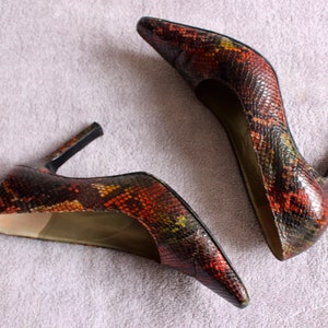 Puede incluir: Un par de zapatos de tac&oacute;n alto con estampado de piel de serpiente en tonos marrones, negros y verdes.