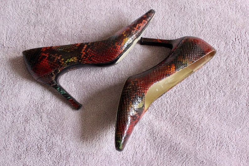 Puede incluir: Un par de zapatos de tac&oacute;n alto con estampado de piel de serpiente en tonos marrones, negros y verdes.