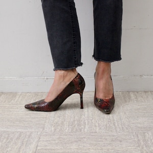 Puede incluir: Un par de zapatos de tac&oacute;n de aguja de piel de serpiente roja, negra y dorada con punta.