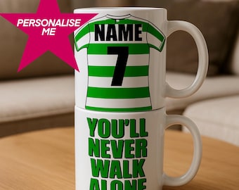May include: Two white ceramic mugs stacked on top of each other. The top mug features a green and white striped jersey design with the number 7 and the word "NAME". The bottom mug has the text "YOU'LL NEVER WALK ALONE" in green.