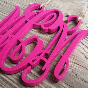 May include: A pink wooden sign with the word "Mom" written in a cursive font.
