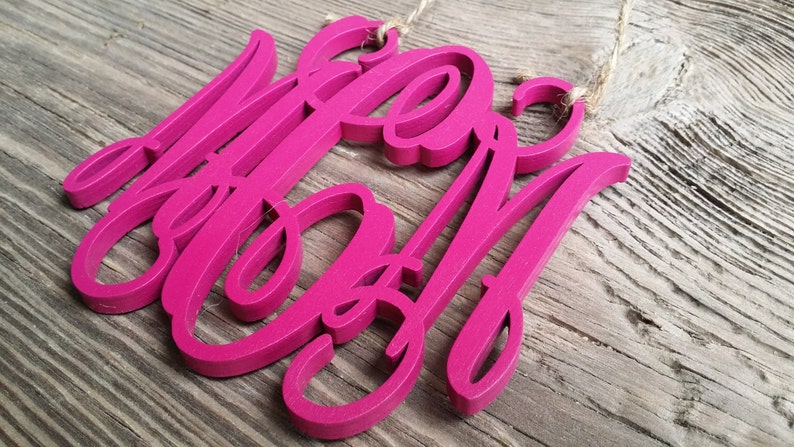 May include: A pink wooden sign with the word "Mom" written in a cursive font.