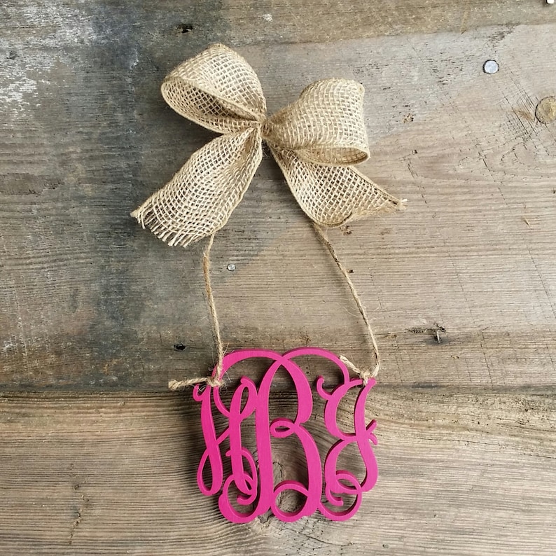 May include: A pink wooden monogram with the letters "HBG" in a cursive font. The monogram is hanging from a piece of twine with a hessian bow.