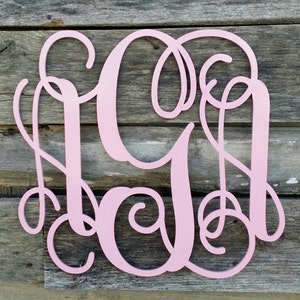 May include: A pink wooden monogram with the letters "SGA" in a cursive script font. The monogram is made of a single piece of wood and has a smooth, painted finish.