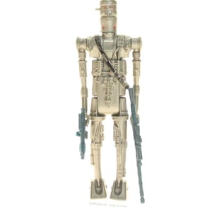 May include: A silver-colored action figure of a robot with a blue blaster in each hand. The robot has a helmet with red eyes and a black strap across its chest.