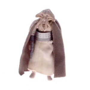 Puede incluir: Figura de acción beige de un personaje de una franquicia de ciencia ficción. La figura tiene una túnica beige, una capa marrón y una cabeza única con múltiples tentáculos. La figura está sobre una superficie blanca.