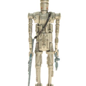 May include: A silver and gray action figure of a robot with a helmet and a blaster in each hand. The robot is standing on a white background.
