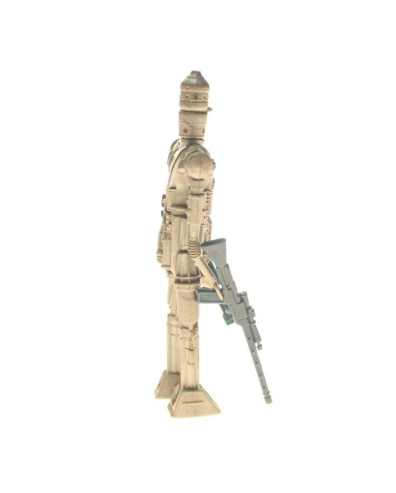 May include: A beige and brown plastic action figure of a Star Wars character, a sandtrooper, holding a black and green blaster rifle.