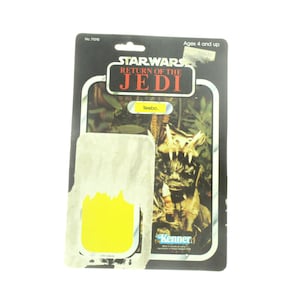 Puede incluir: Una tarjeta de figura de acción vintage de Star Wars con Teebo de El Retorno del Jedi. La tarjeta es negra con una pegatina amarilla en la parte delantera. La tarjeta tiene el logotipo de Kenner y el texto "Star Wars El Retorno del Jedi" y "Teebo."