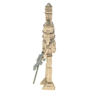 May include: A white plastic action figure of a Star Wars character, a droid, holding a blue and gray blaster rifle. The droid has a white helmet with a black visor and a white body with black details.