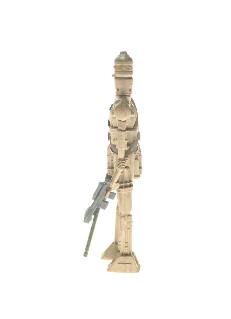 May include: A white plastic action figure of a Star Wars character, a droid, holding a blue and gray blaster rifle. The droid has a white helmet with a black visor and a white body with black details.