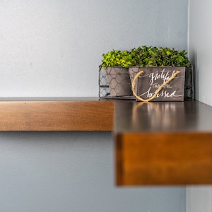 Op de afbeelding: Een houten plank met een draadmand waarin twee kleine potplanten staan. De mand heeft ook een klein bord met de tekst "Grateful, Thankful, Blessed".
